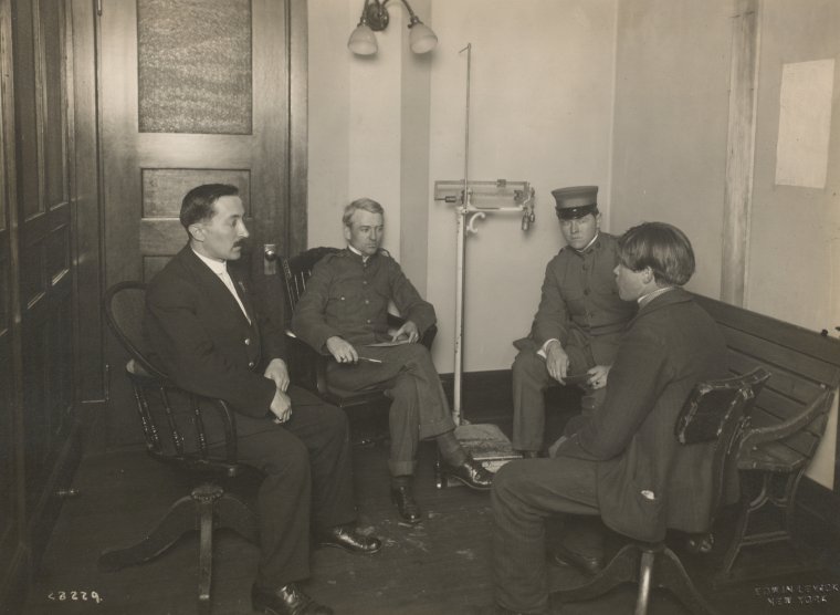 A private interview between a young immigrant and an Ellis Island official. Two staff members [?] are also present., Digital ID 1693107, New York Public Library