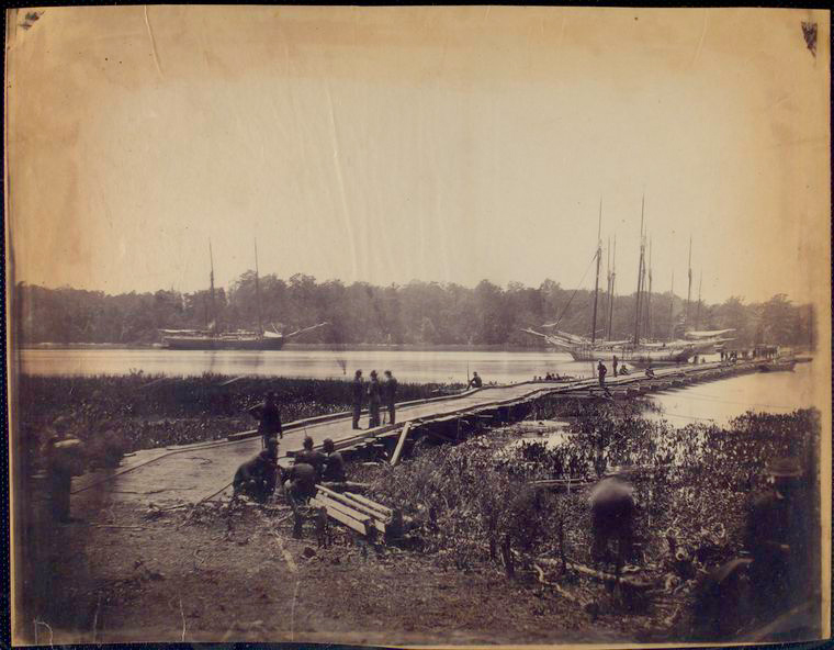 Pontoon bridge, across the James, June 1864.,Pontoon bridge across the James [Men sitting and standing in foreground, ships at anchor in river]., Digital ID 1150142, New York Public Library