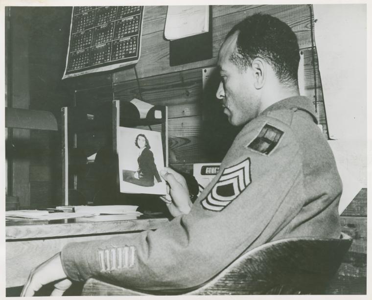 A soldier will take a bride.,[African American Master Sergeant William P. Thompkins sitting at a desk and looking at a photograph of his fiancée Delores Taylor that he holds in his right hand, Fort Dix, New Jersey, April 2, 1947.] , Digital ID 1260315, New York Public Library