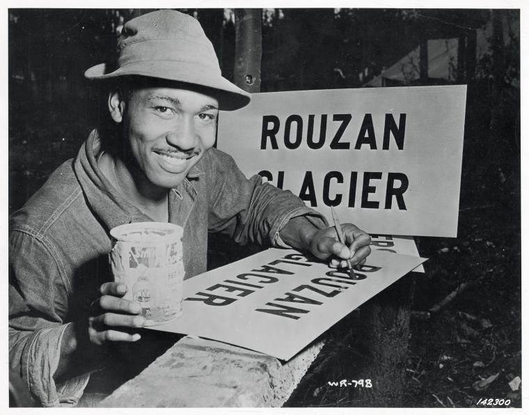 [African American Private First Class William Hughes of the U.S. Army Engineers painting a sign reading "Rouzan Glacier," 1942.],Alcan Highway under construction., Digital ID 1260427, New York Public Library