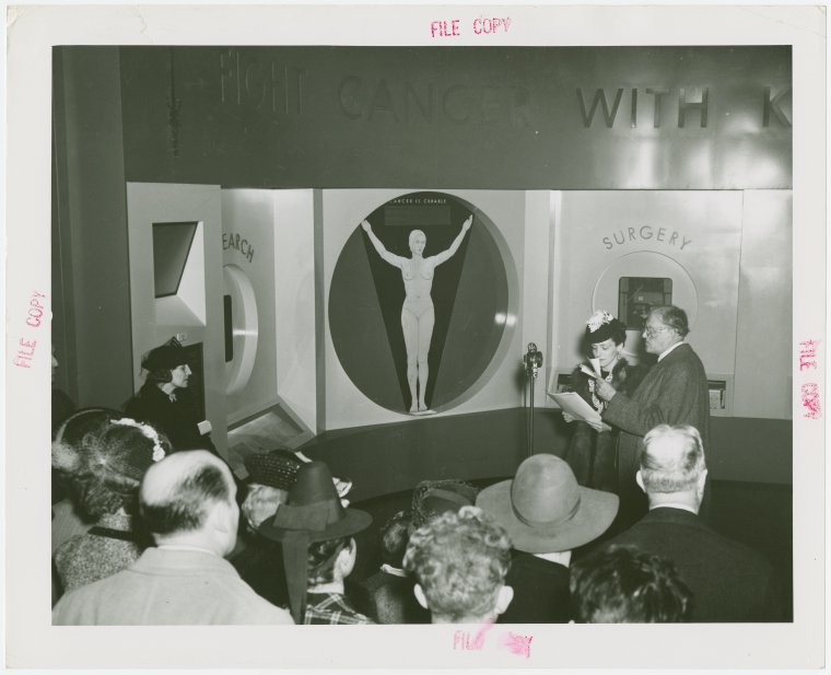 Medicine and Public Health - Man and woman speaking to crowd at exhibit on cancer treatments, Digital ID 1677859, New York Public Library