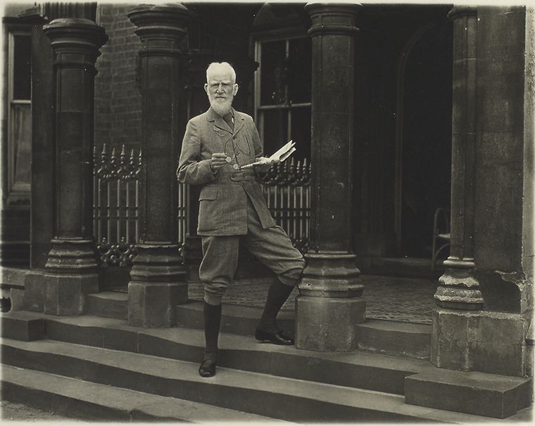 Bernard Shaw on the steps with a news-paper in his hands., Digital ID 482973, New York Public Library