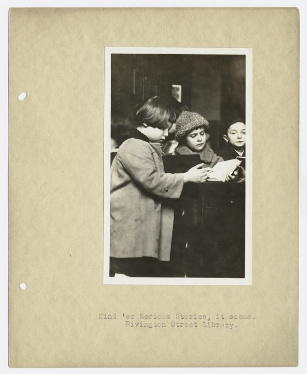 Children standing and reading.  "Kind 'er Serious Stories, it seems.  Rivington Street Library.", Digital ID 94801, New York Public Library