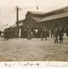Postcard of large group of people walking down a cobble-stoned embankment for baptism, warehouse in background.