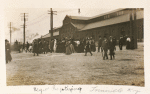 Postcard of large group of people walking down a cobble-stoned embankment for baptism, warehouse in background.