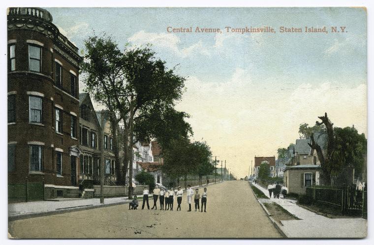 Central Avenue, Tompkinsville, Staten Island, N.Y. [residential street with row homes and interesting 3-story brick apt.? building; people walking on street and ten children posed in a line in street]. Image ID: 105105