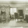 A New England bedroom of about 1800, showing four poster with curtains and valance, and truckle bed to be pulled out from beneath larger bed.