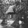 Homeward bound. ; [Woman with children standing outside dwelling.]