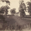 Group of men seated and standing on grass near road; chapel and other buildings in rear.