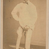 Man stands against metal support, exhibiting injured right leg; his arched foot rests on block