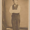 Man with injured right leg stands clothed in shirt, vest and pants, with arms crossed
