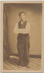 Man with injured right leg stands clothed in shirt, vest and pants, with arms crossed