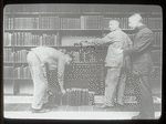 Three men at dusting books, one bent over