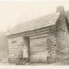 Woman and girl standing on the steps of a log cabin.