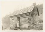 Woman and girl standing on the steps of a log cabin.