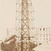 Scaffolding for the assemblage of the Statue of Liberty, of which the head is shown at left, in Paris