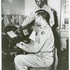Corporal Parkins D. Peck, chief teletype operator, seated at the teletype machine while African American Private James Lee stands behind him and points to a Western Union telegram form, Camp Edwards, Kentucky