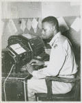African American Private James C. Lee sitting at a teletype machine in the telegraph room at Camp Edwards, Kentucky