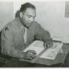 African American First Lieutenant Seth Finley seated at a desk and holding a ruler over a stack of papers, Fort Lewis, Washington
