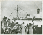 African American members of the 343rd ASF Band playing saxophones next to a crowd of women waving and welcoming the arrival of the last members of the 93rd Infantry Division