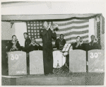 Group portrait of African Americans, Seabee Band members, from the 30th Special U.S. Naval Construction Battalion, playing on a stage