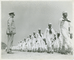 African American recruits in sailor uniforms walking in rows and passing in review before Lieutenant Commander Daniel W. Armstrong