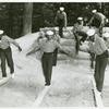 Three African American sailors walking across and trying to balance on wooden beams that are laid across a sand pit while others look on and wait their turn at U.S. Navy Receiving Station, Camp Robert Smalls
