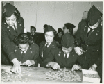 Two African American Lieutenants of the Women's Army Corps sitting at a table and working on jigsaw puzzles while three others assist and look on
