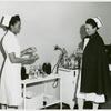 Captain Mary L. Petty, Chief Nurse, holding a glass bottle and showing it to 2nd Lieutenant Olive Bishop, who is writing on a small pad of paper