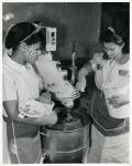 Female African American workers assisting each other at the dough mixer in food processing shop