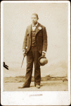 Full length portrait of man with bowler hat and cane.