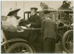 Unidentified man and woman sitting opposite one another in a motorcar.