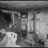 Man in kitchen—bedroom with dishes, clothes, irons (1904).