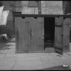 Outhouses and woman scrubbing a rug (1905).