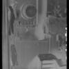 Interior of room: chair, shelf with comb, brush, lamp, bottles, clothing