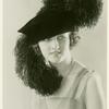 Woman modeling elaborate feathered hat.