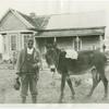 Man with mule in front of farmhouse