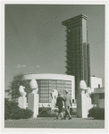 Glass Center - Man and woman walking through Baboon Fountain toward building