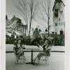 Sports - Ice Skating - Man on ice skates jumping over two chorus girls sitting at table