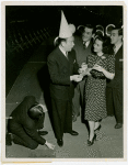 Ticket Sales - Fred Allen selling ticket books to woman and two men while other man lights match from his shoe