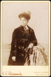 Studio portrait of woman wearing hat, and velvet coat.
