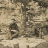 Frederick V. Field and two others eating a picnic meal in the woods with a horse in the background