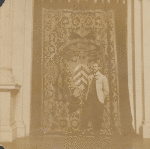 Man in light colored coat in front of tapestry