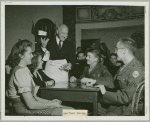 Mr. Cecil B. DeMille serving coffee to service men seated with hostesses