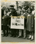 Mixed race group of children carrying sign: "No Child is Free Until ALL are Free," circa late 1950s