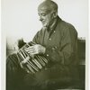 Henry Cowell trying out one of the five tablas for the tablatarang (= circle of tuned drums) presented to him for his Symphony No. 13 (Madras) by the Music Academy of Madras, India.  NYC, 1959