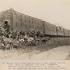 General view of construction train in rear hauling ties and rail. Seats in buckboard, John Grant, time keeper. Standing, Donald Grant, contractor, J.H. Benson, supt., Mr. Cox, paymaster, the camp doctor and a visiting Indian.