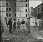 Contact sheet of pre-production location shooting with stand-ins. Vacant lot with three women and two men standing on tar paper with crew at perimeter of shot