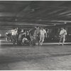 Jerome Robbins, crew, dancers: Underground parking garage: crew pulling cameramen on dolly, Robbins running along side dancers moving toward camera crew