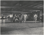 Jerome Robbins, crew, dancers: Underground parking garage: crew pulling cameramen on dolly, Robbins running along side dancers moving toward camera crew